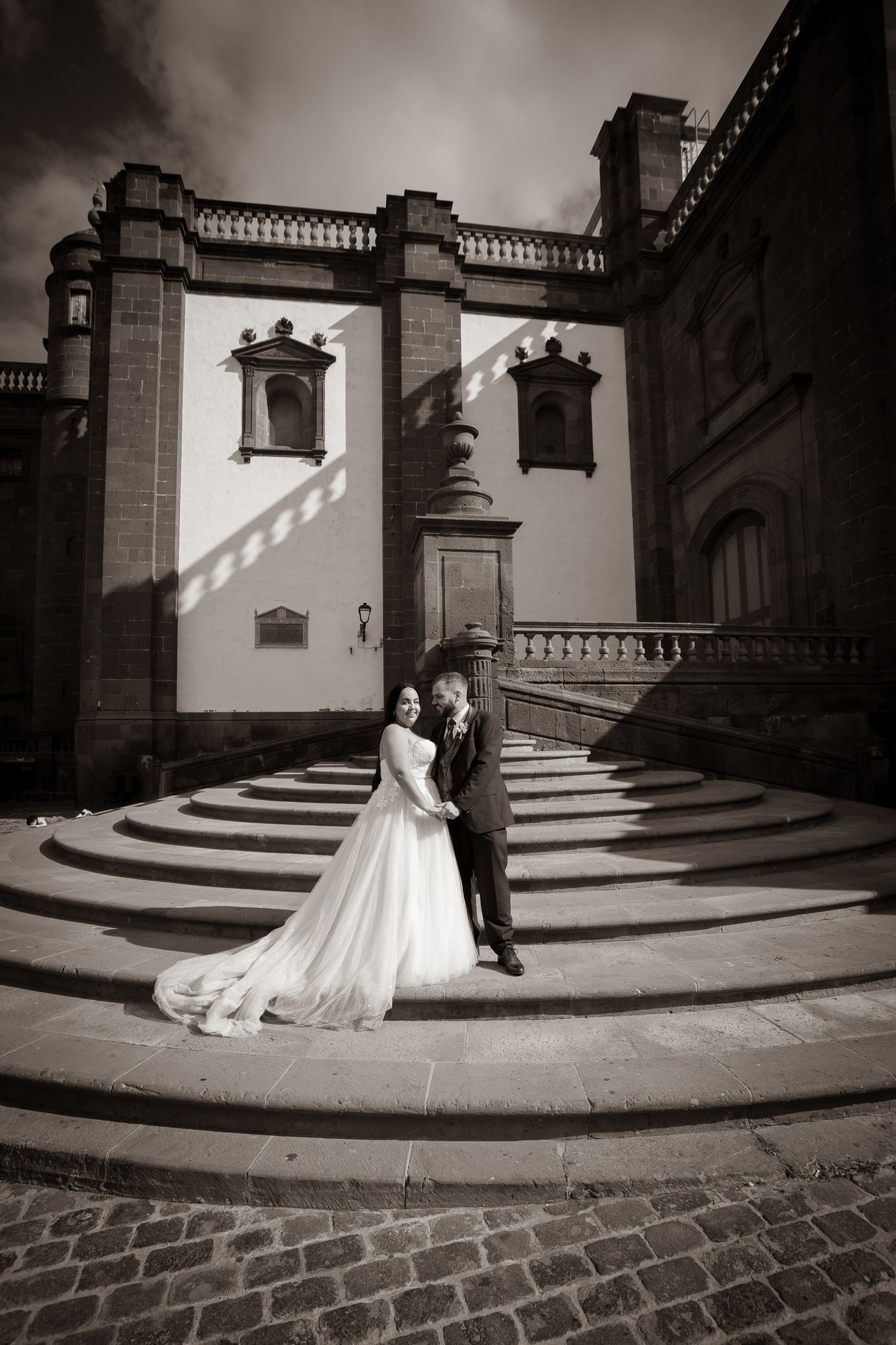 Black and white wedding photos on curved stone steps of historic building.