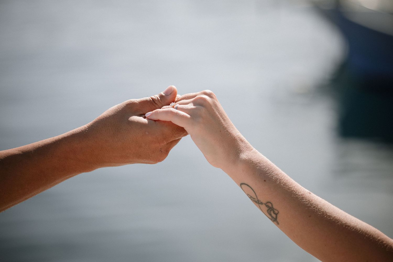Close-up shot of two hands reaching towards each other with a wedding ring and delicate tattoo visible.