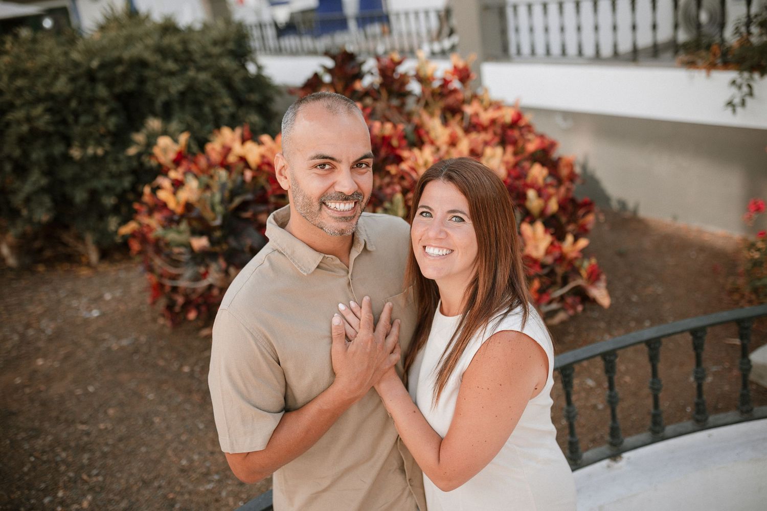 Couple sharing joyful moment among autumn-colored foliage and white picket fence.