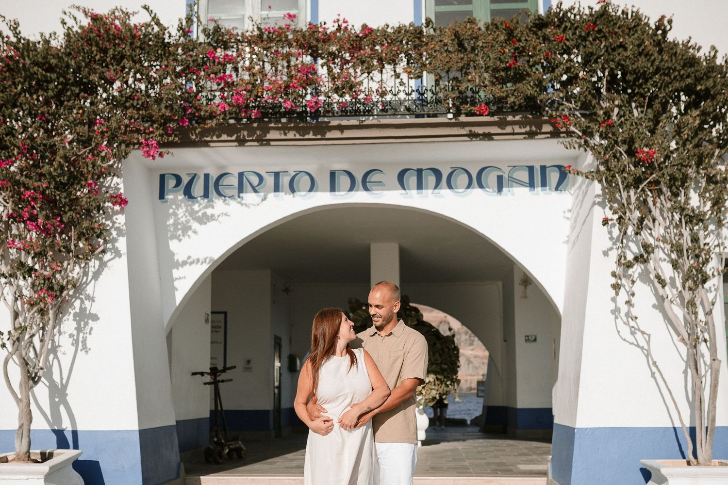 Mediterranean style marina entrance with flowering bushes and white archways.