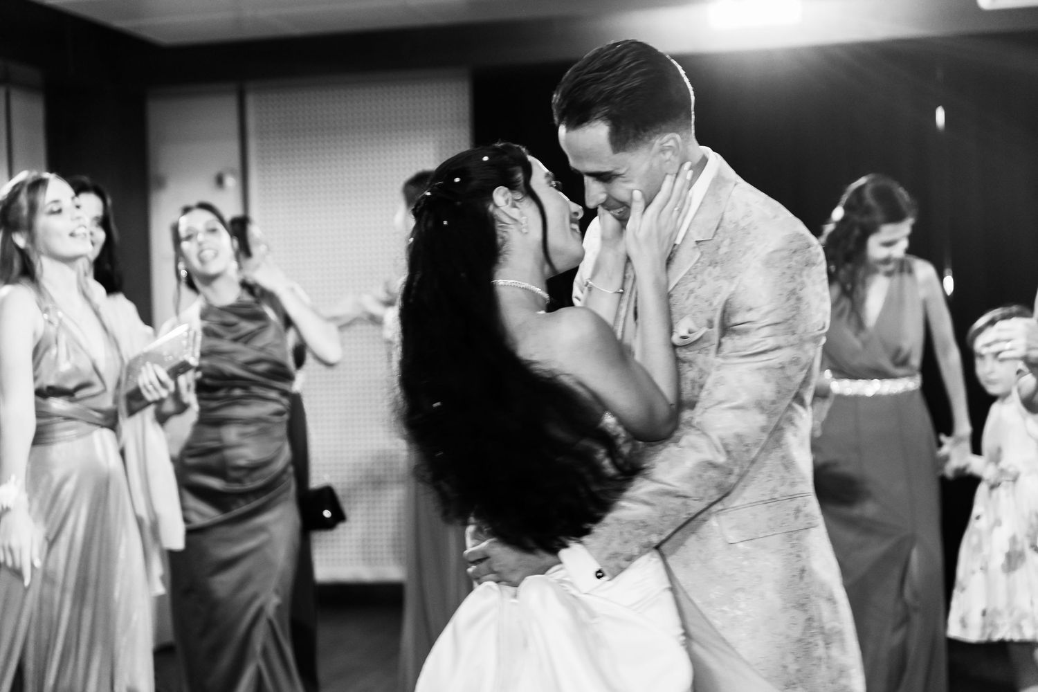 Black and white photo of a joyful wedding celebration with dancing and embracing.