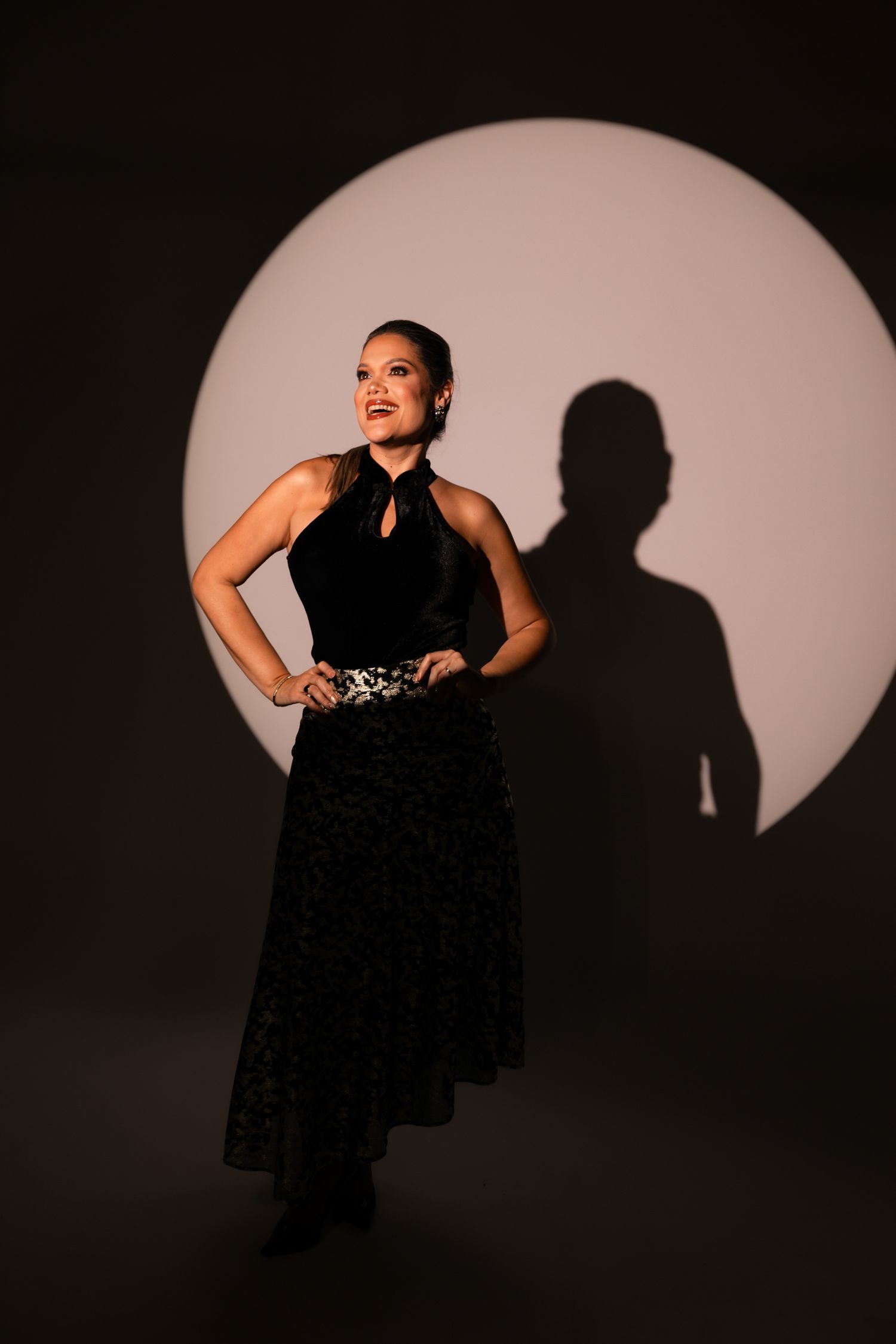 Dramatic series of silhouettes showing a performer in a black dress against a circular spotlight background.