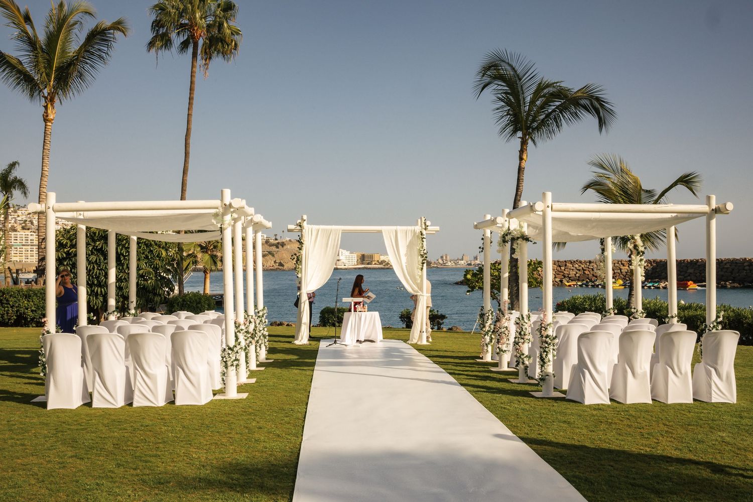 Tropical beach wedding venue with palm trees and white-draped ceremony structures.