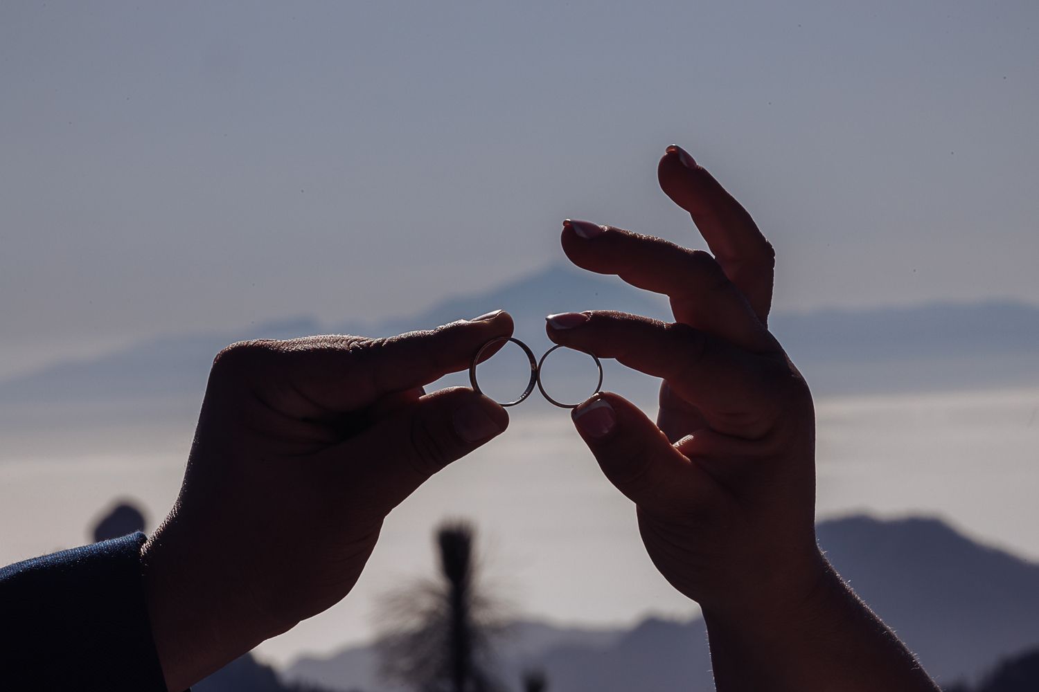 Silhouetted hands reaching toward each other against a bright mountain sky.