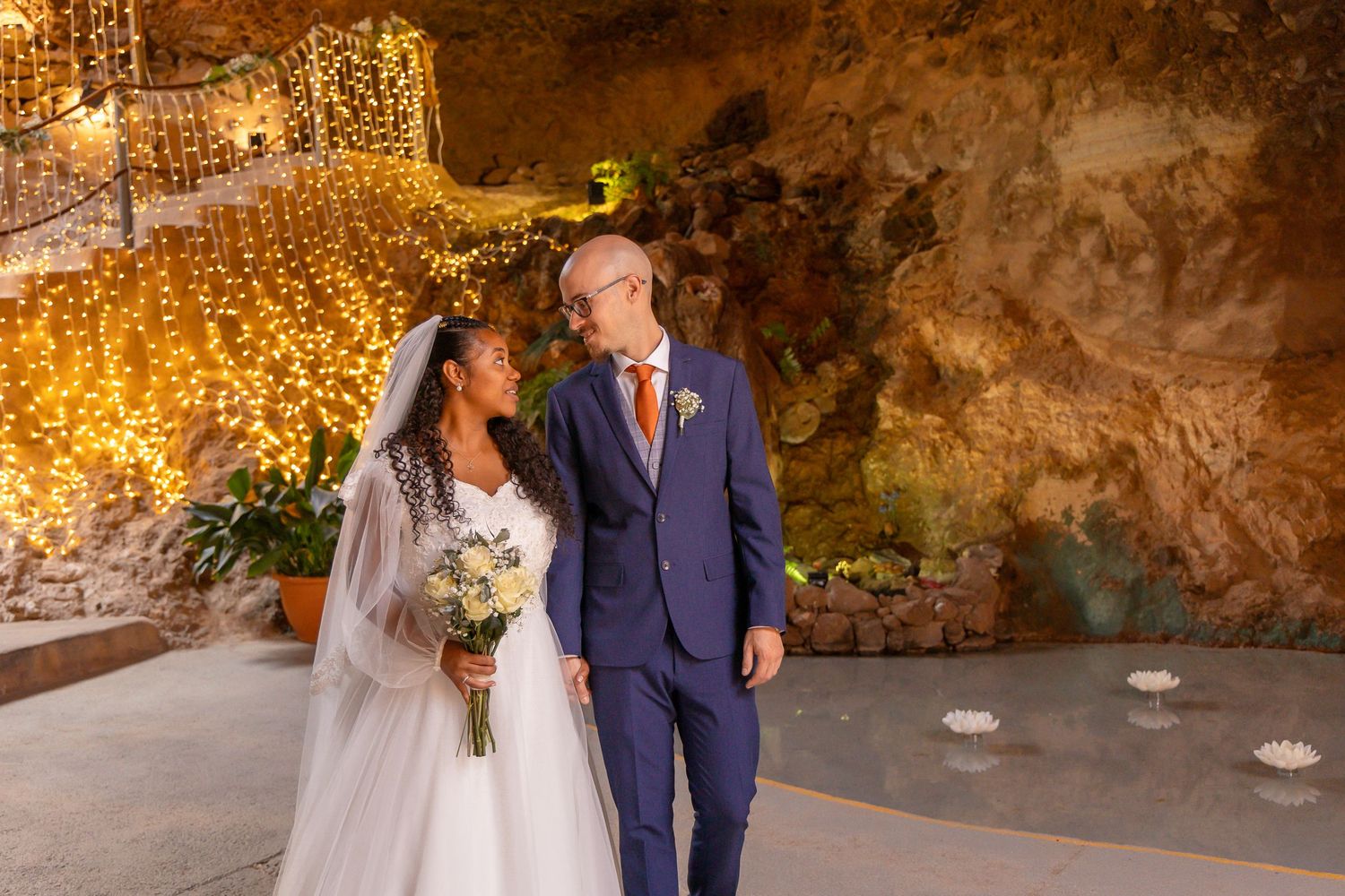 Wedding couple poses in romantic cave setting with glowing fairy light backdrop.