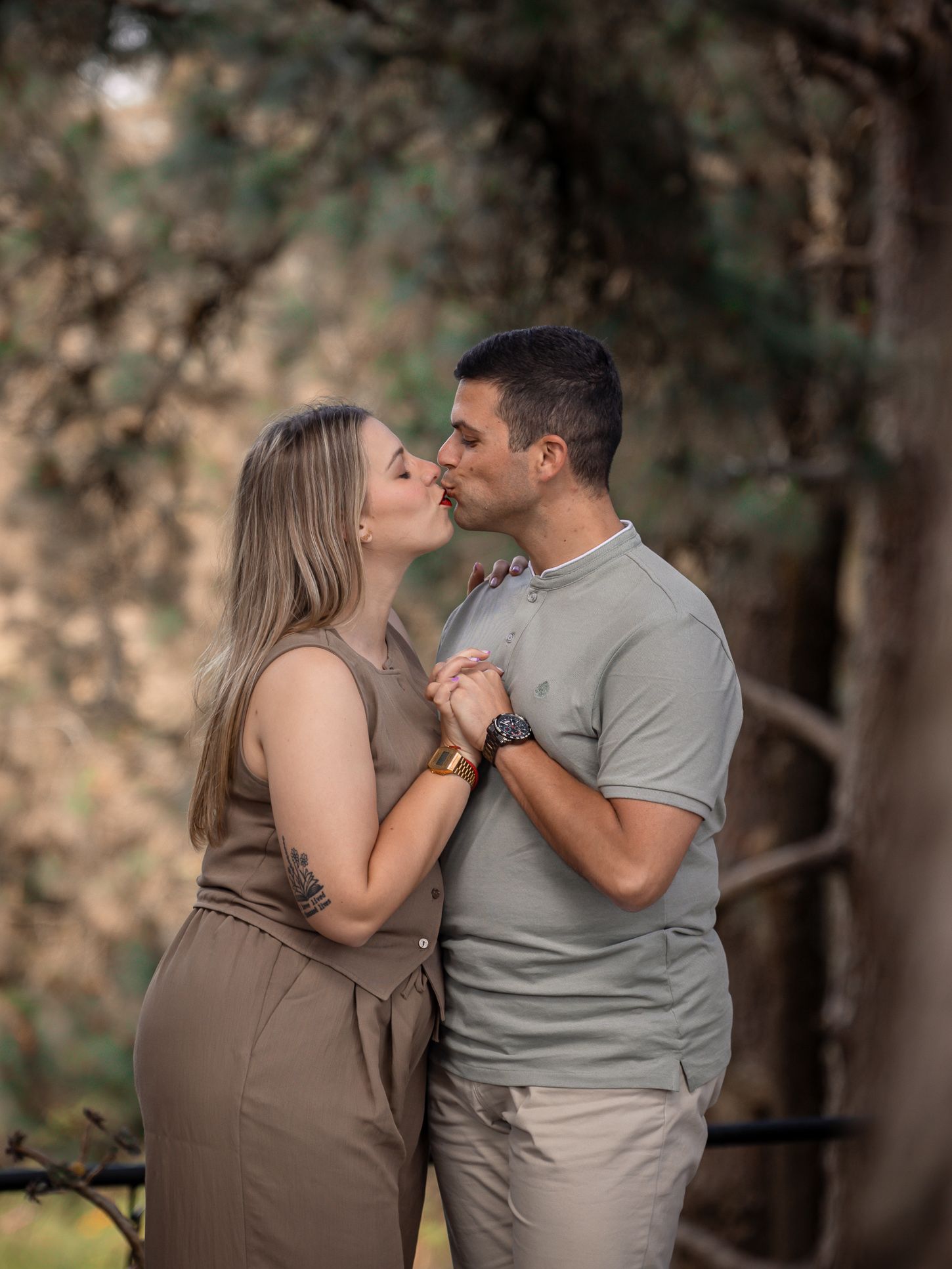 A couple shares an intimate moment in a wooded area with soft natural lighting.