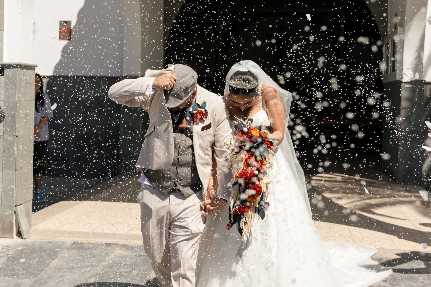 Wedding party celebrates with confetti toss outside church entrance.