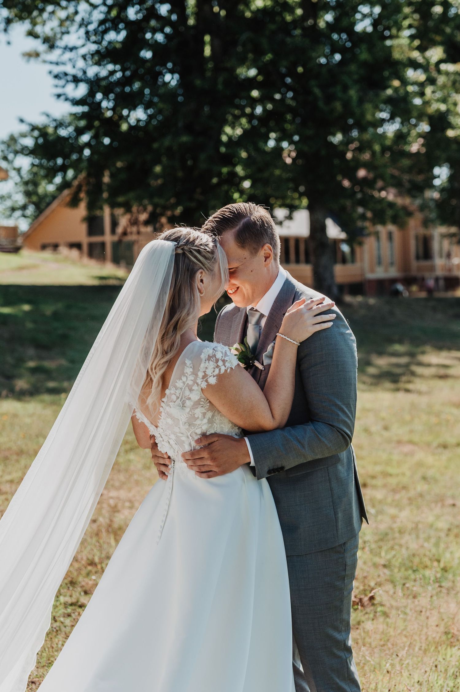 Bride and groom share a romantic moment outdoors, bride in white gown with veil, groom in gray suit.