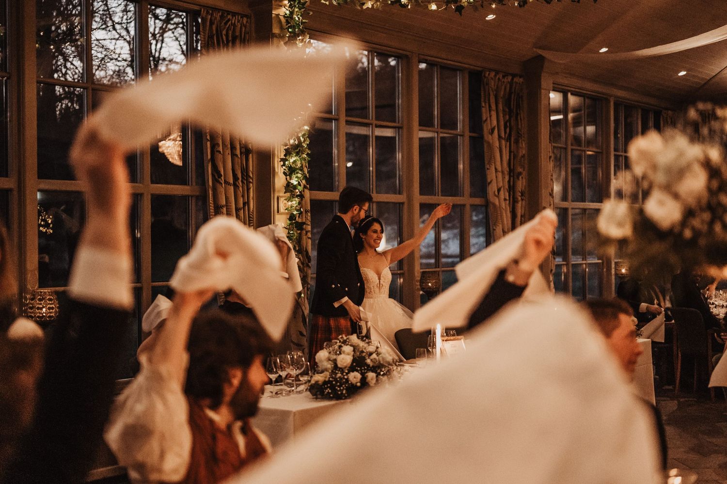 Guests wave white napkins as bride and groom make their grand entrance at an elegant wedding reception.