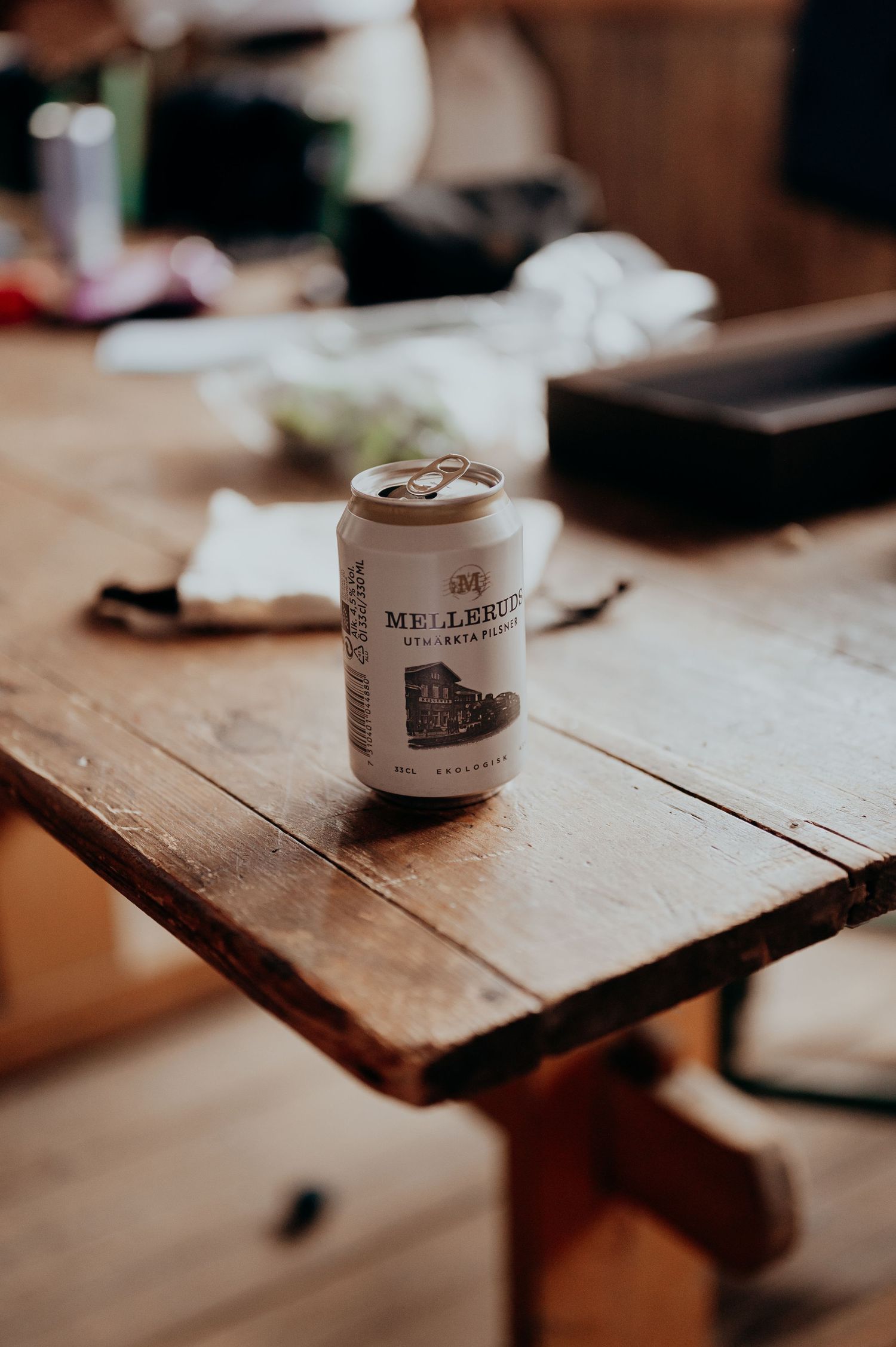 A can of Mellerud beer sitting on a rustic wooden table in a warmly lit room.