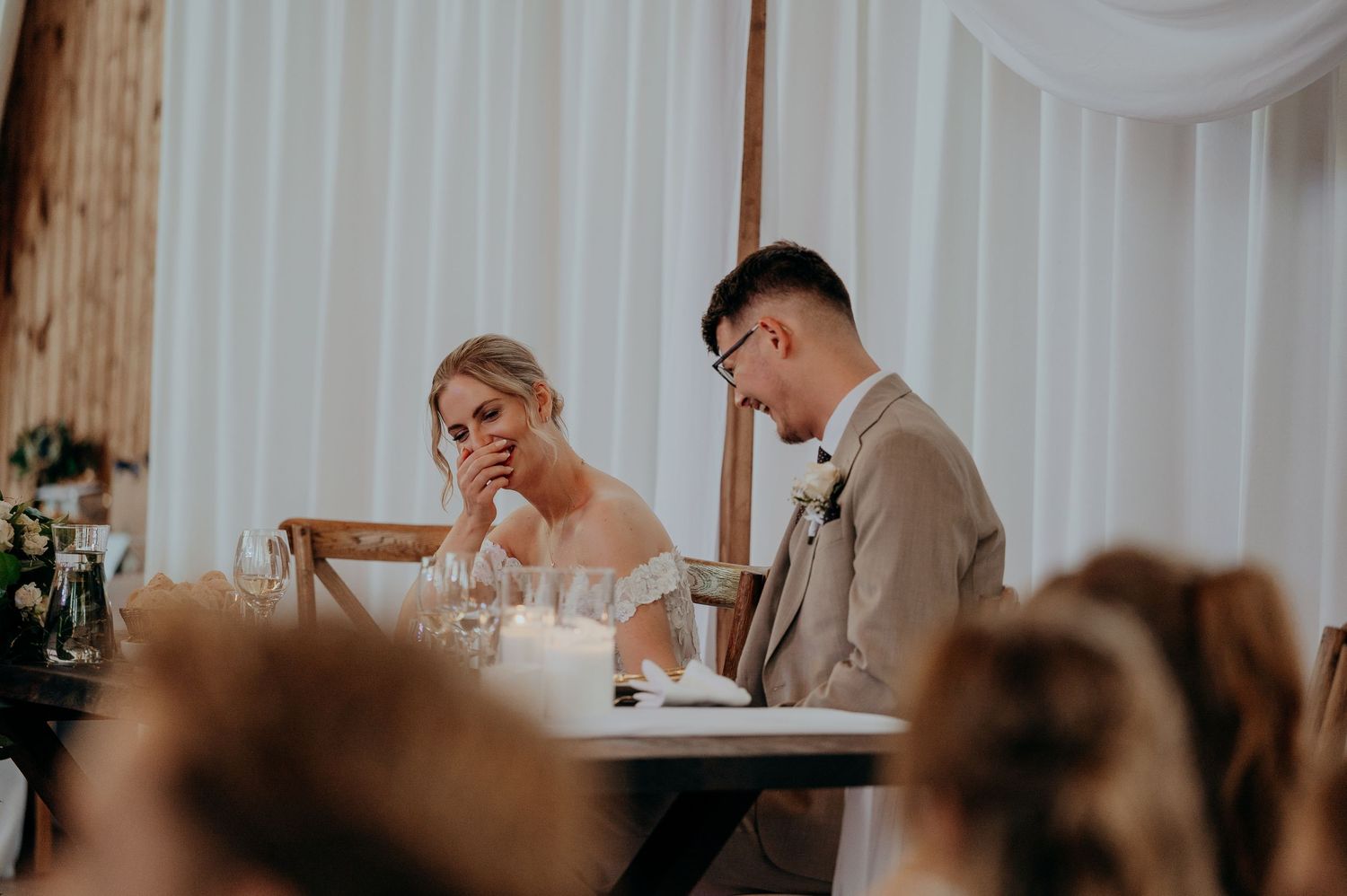 Bride and groom sitting together emotionally at wedding reception head table.