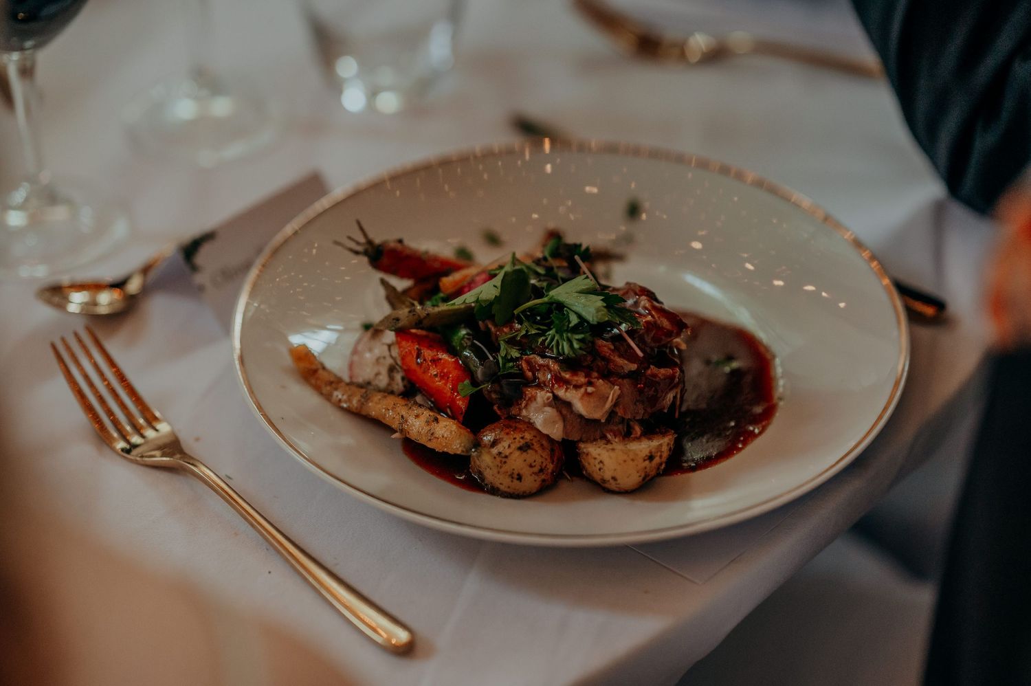 Elegant restaurant plate with roasted meat, vegetables, and rich sauce on white china, fine dining setting.