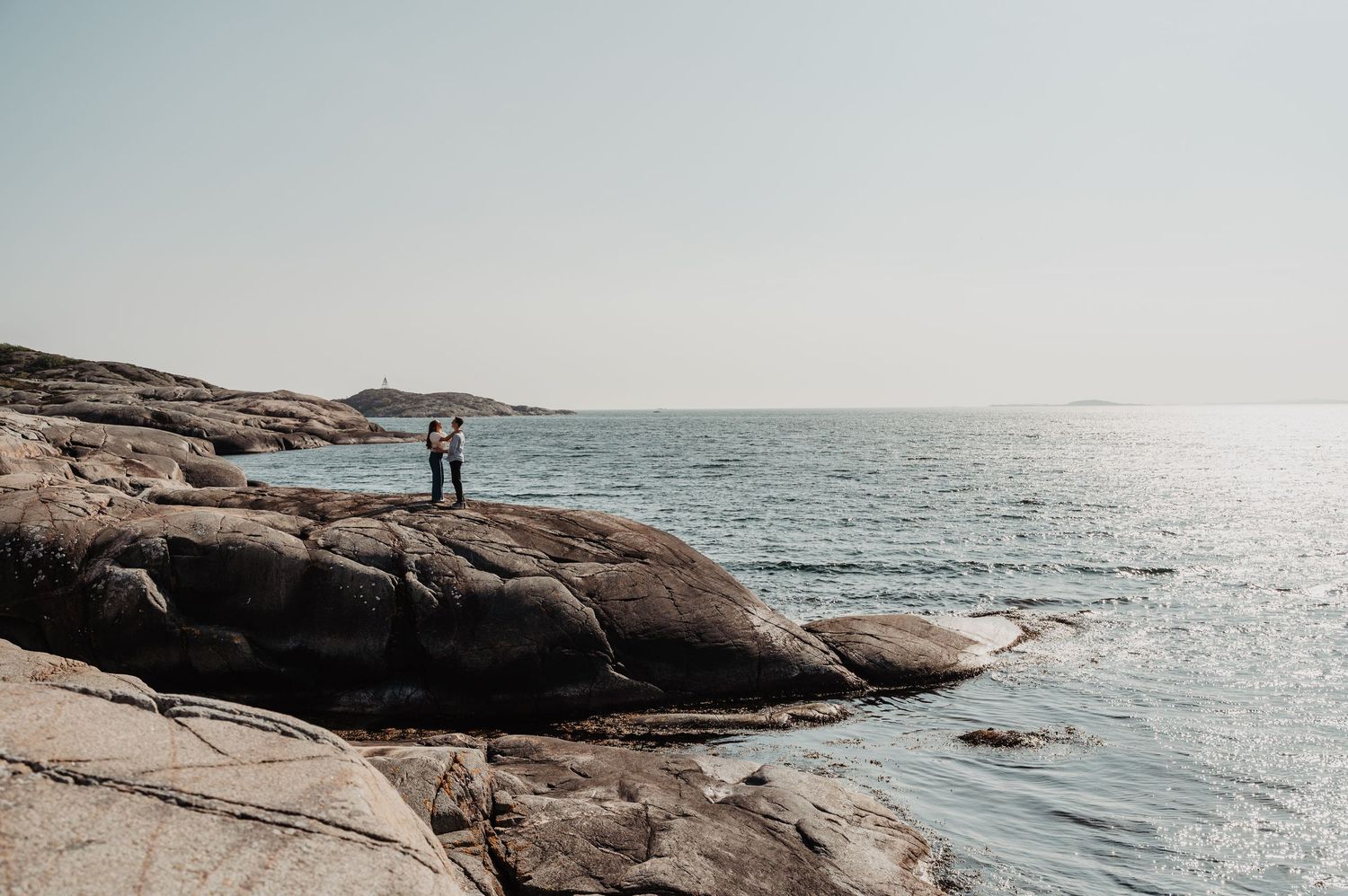 Two people standing together on dramatic rocky coastal landscape with calm sea horizon view.