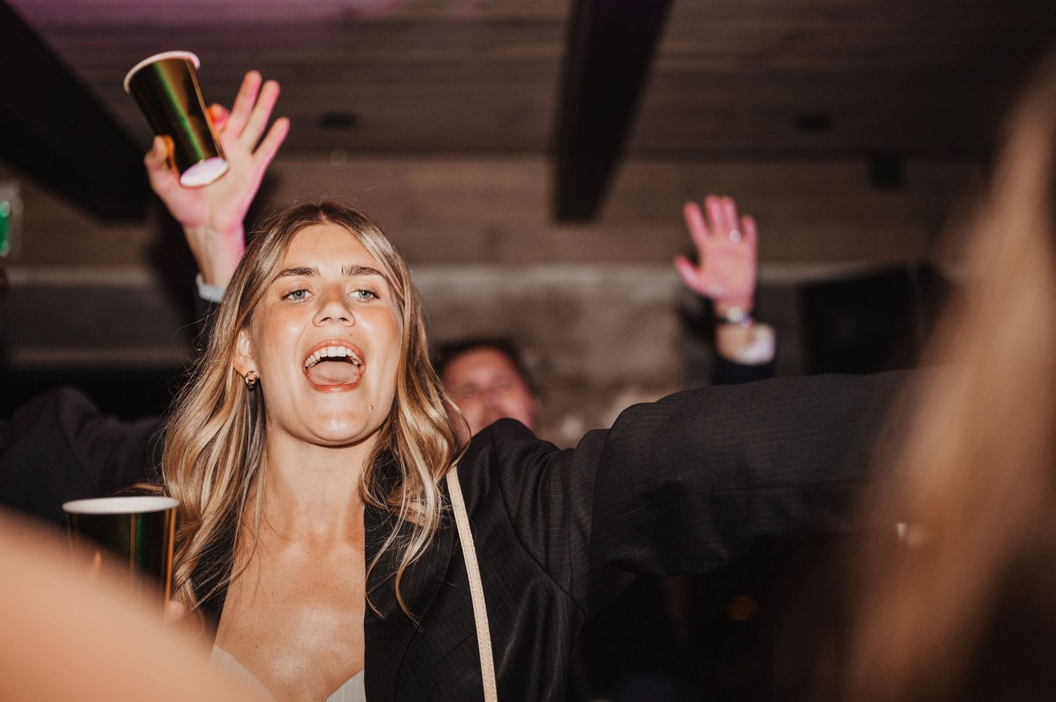 Excited wedding guest raising a drink and singing along on the dance floor.