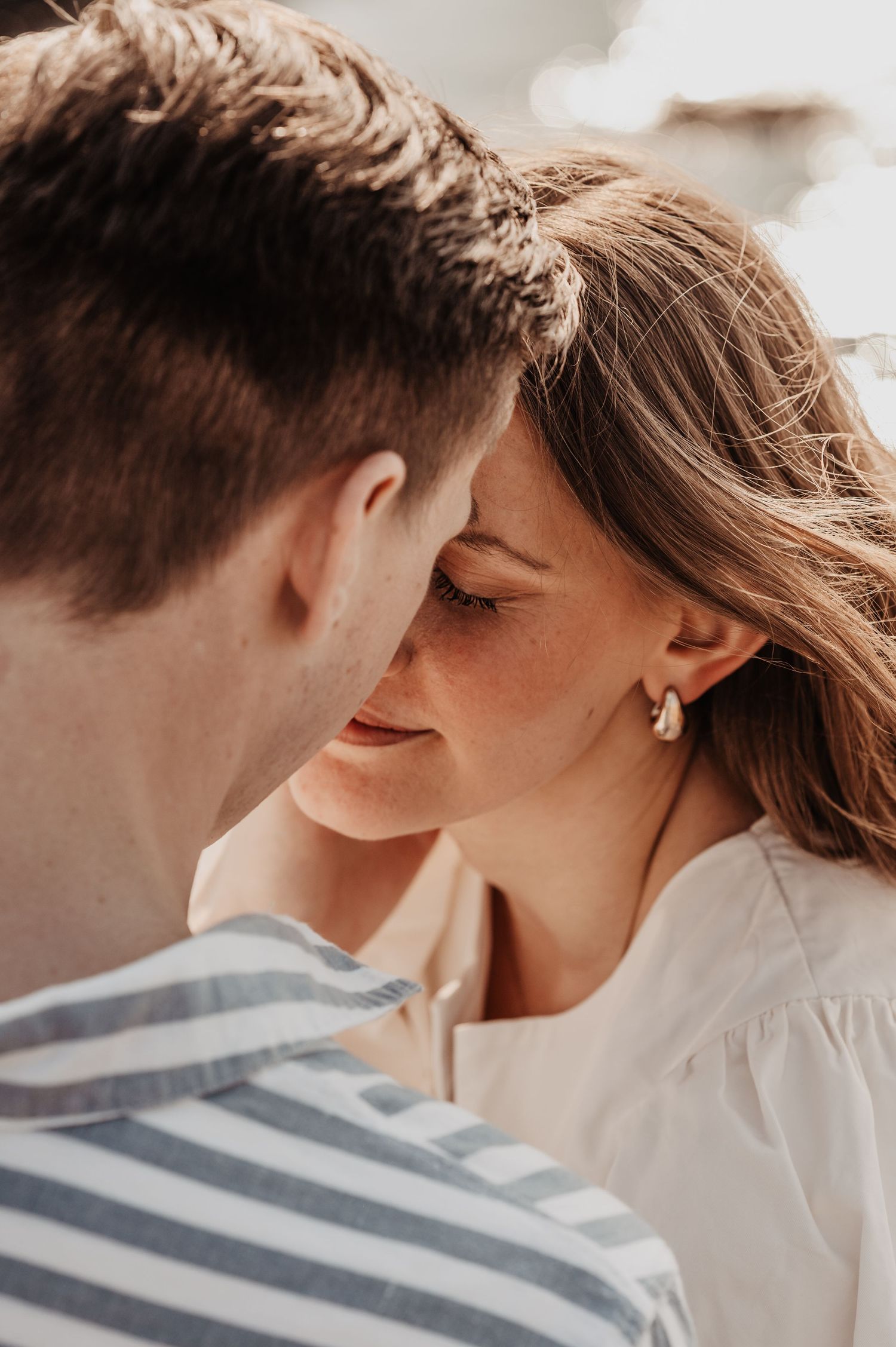 Close-up of a couple nearly kissing, woman with freckles and hoop earring smiling softly.