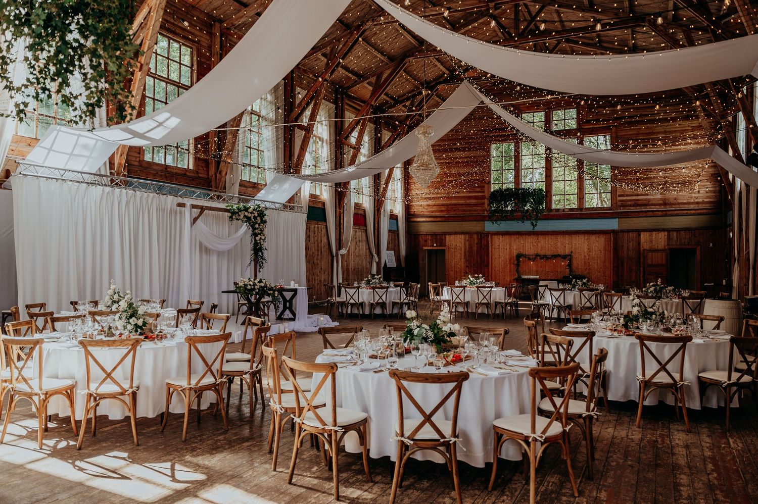 Elegant rustic barn wedding reception with white draping, string lights, and round tables.