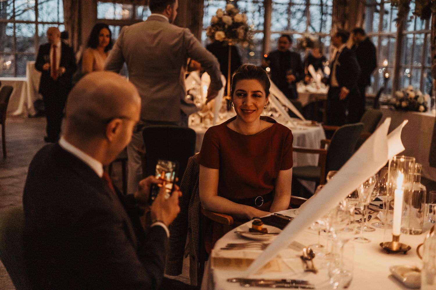 Elegant wedding reception dinner with guests toasting champagne at candlelit tables in a sophisticated venue.