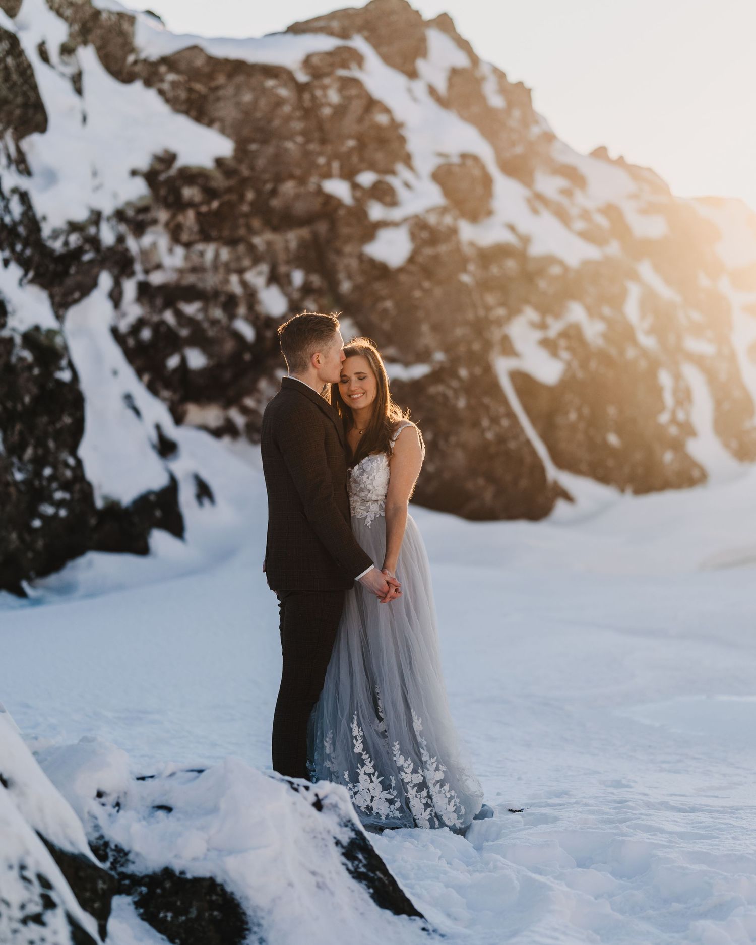 Couple embracing in snowy mountain landscape at golden sunset in a winter wedding elopement.