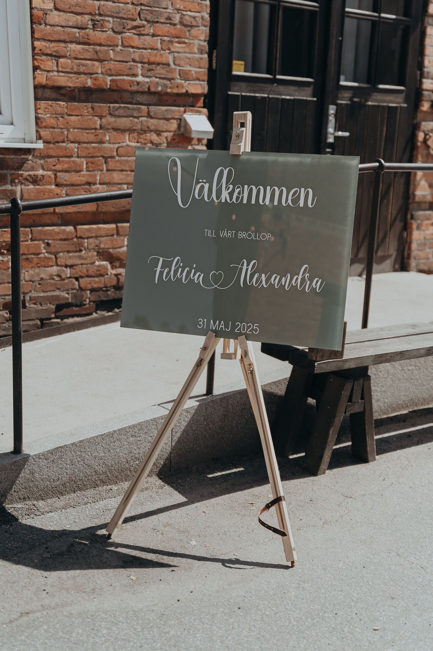 Wedding welcome sign reading Valkommen for Felicia and Alexandra on May 31 2025 outside brick building.