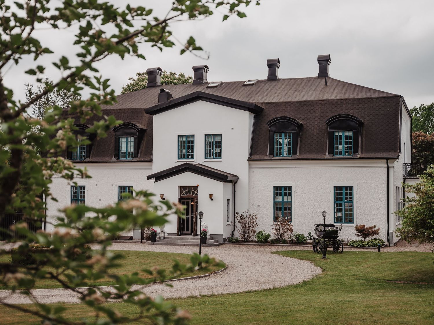 A grand white manor house with dark roof and manicured grounds serves as a wedding venue.