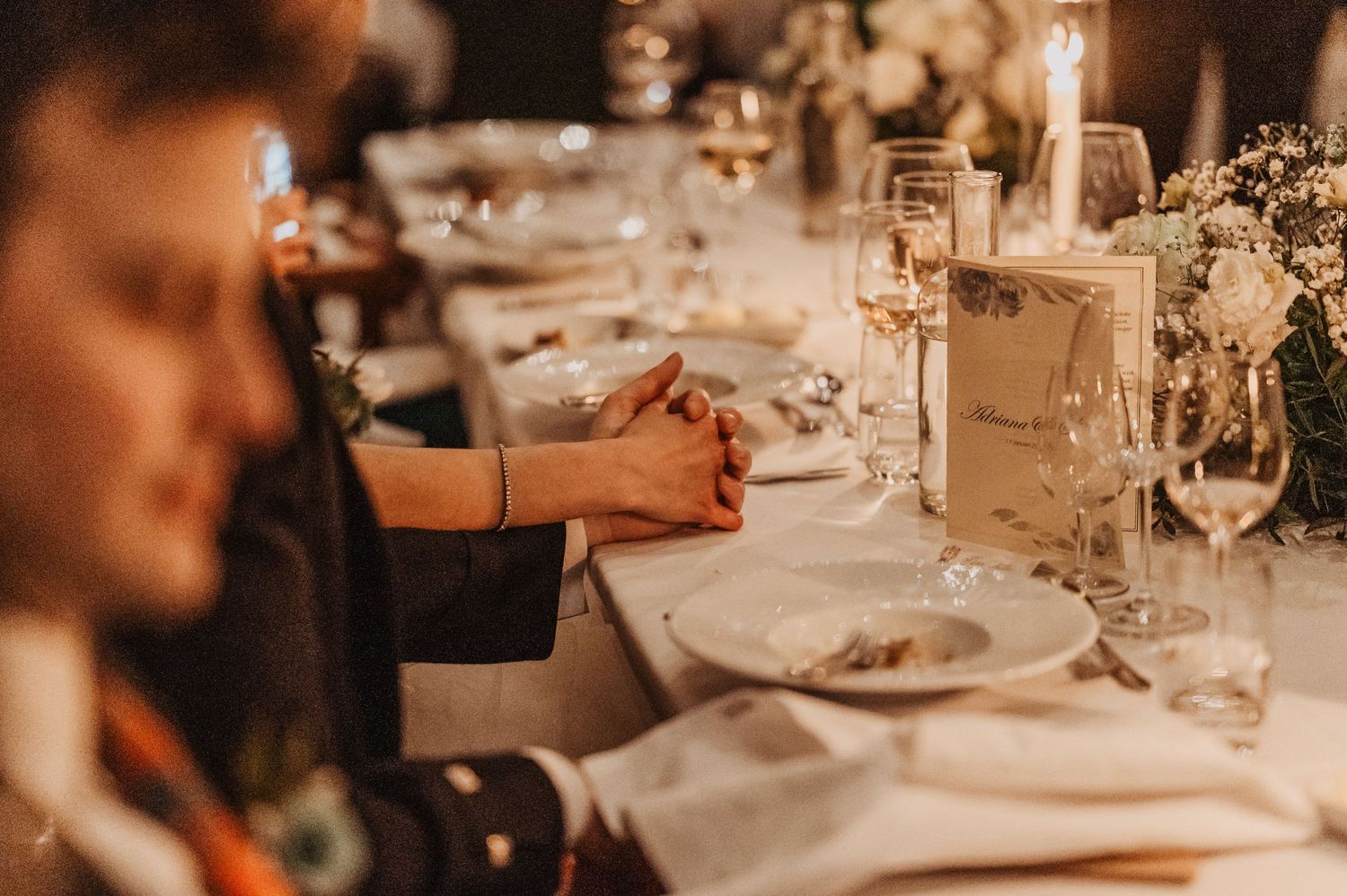 A series of elegant table settings at a formal event with white linens and glassware in warm ambient lighting.