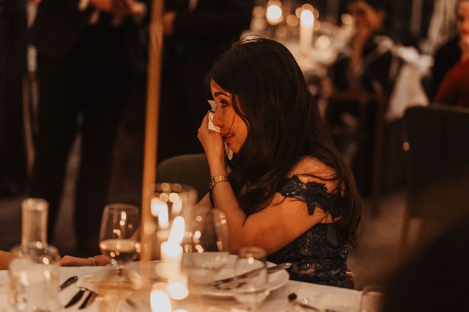 Candlelit wedding reception tables decorated with elegant place settings and glowing lanterns in a dimly lit venue.