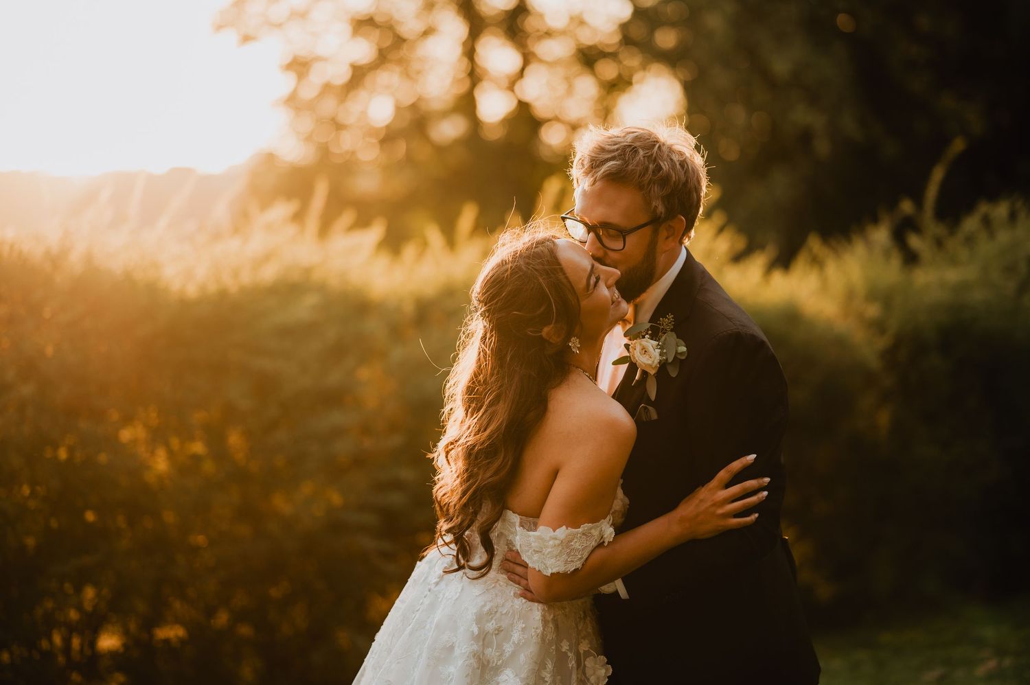 Bride and groom sharing romantic golden hour kiss in lush garden at sunset.