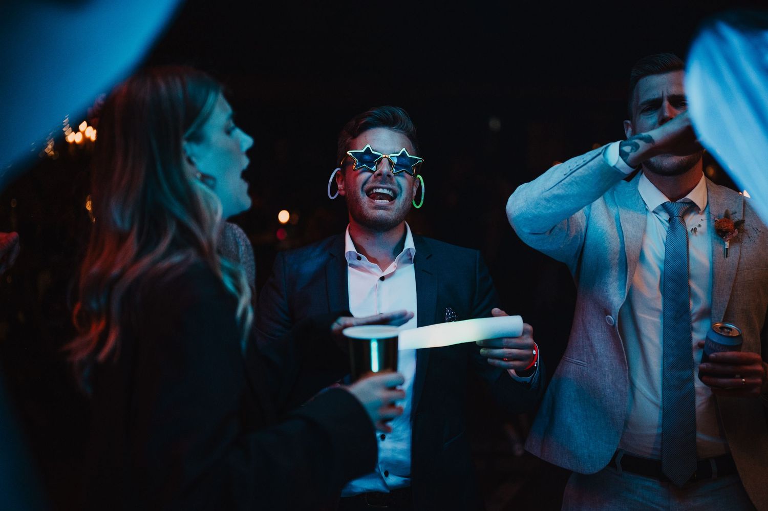 Wedding guests laughing and wearing novelty sunglasses during a fun evening reception.