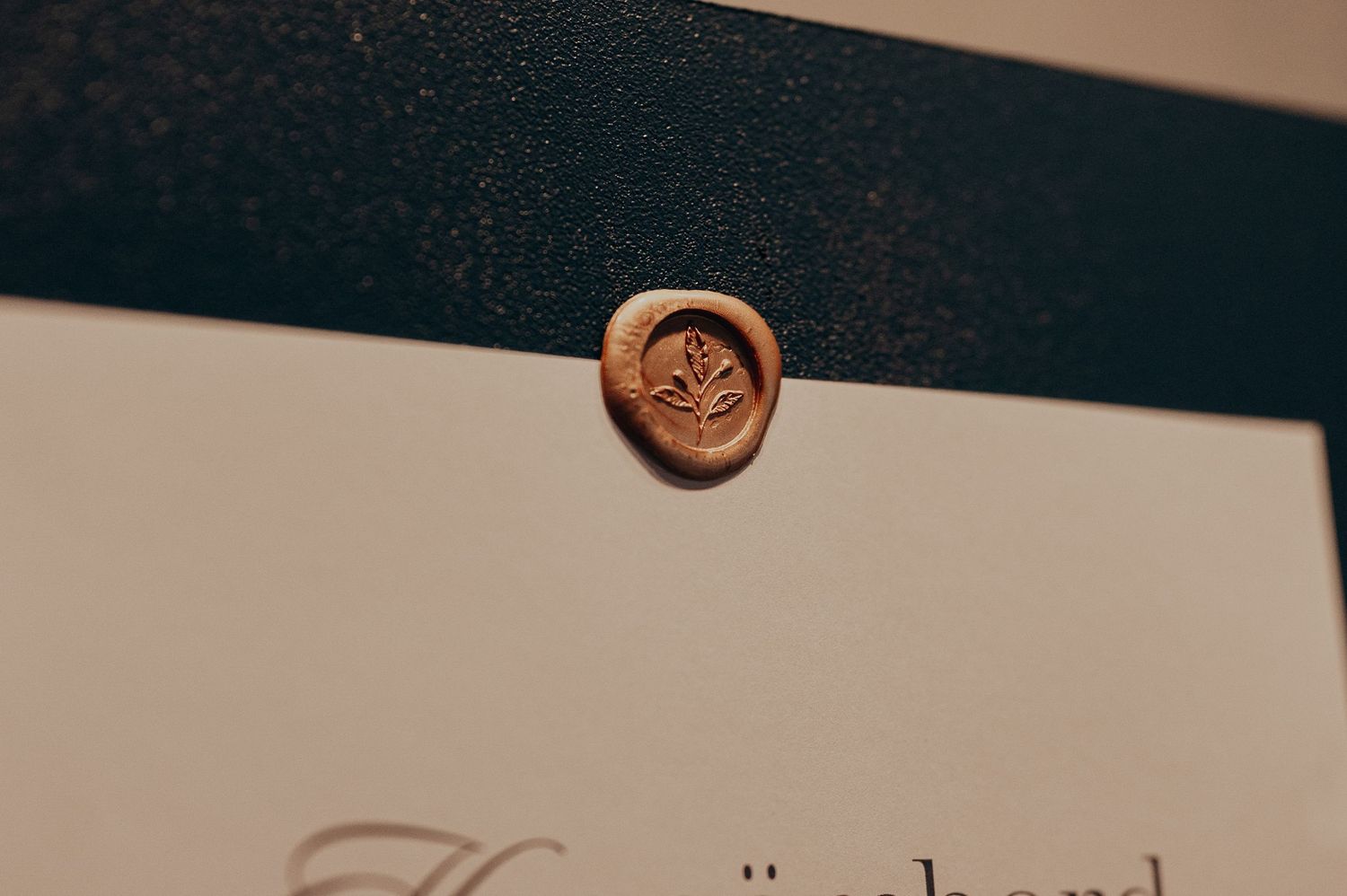 Close-up of copper wax seal with floral motif on elegant dark wedding stationery invitation.