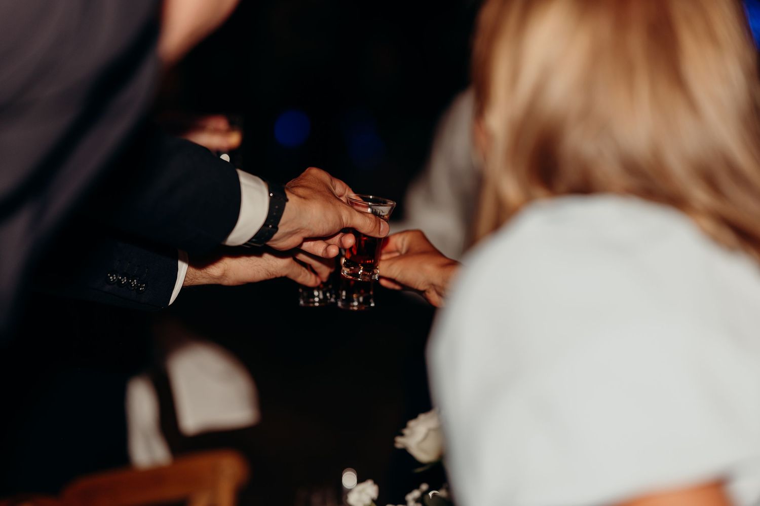 Wedding guests clinking shot glasses together in a celebratory toast at reception.