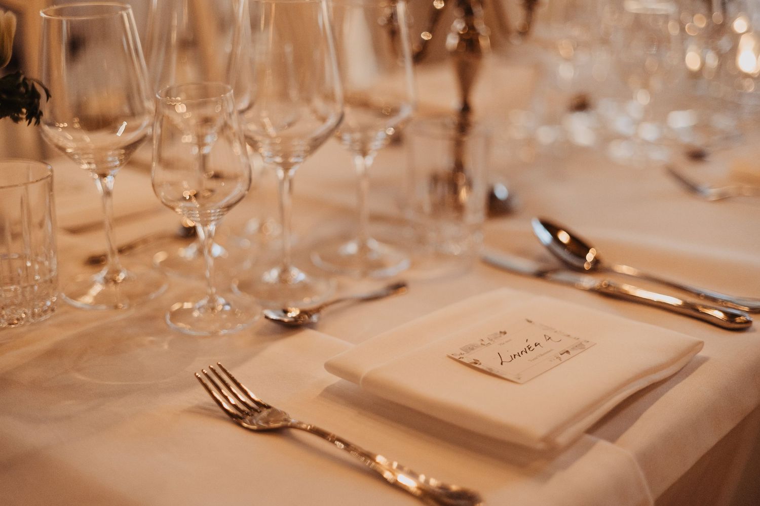 Elegant wedding table setting with crystal wine glasses, silver cutlery, and a white napkin place card on ivory linen.