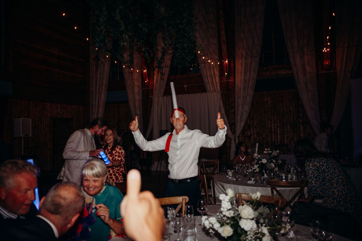 A joyful guest dances with sparklers at an elegantly decorated indoor wedding reception with string lights.