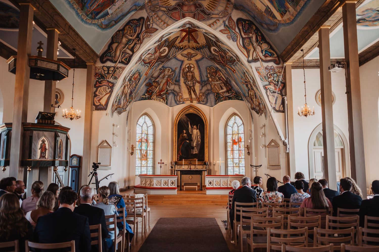Beautiful painted vaulted ceiling church interior with wedding guests seated in wooden pews.