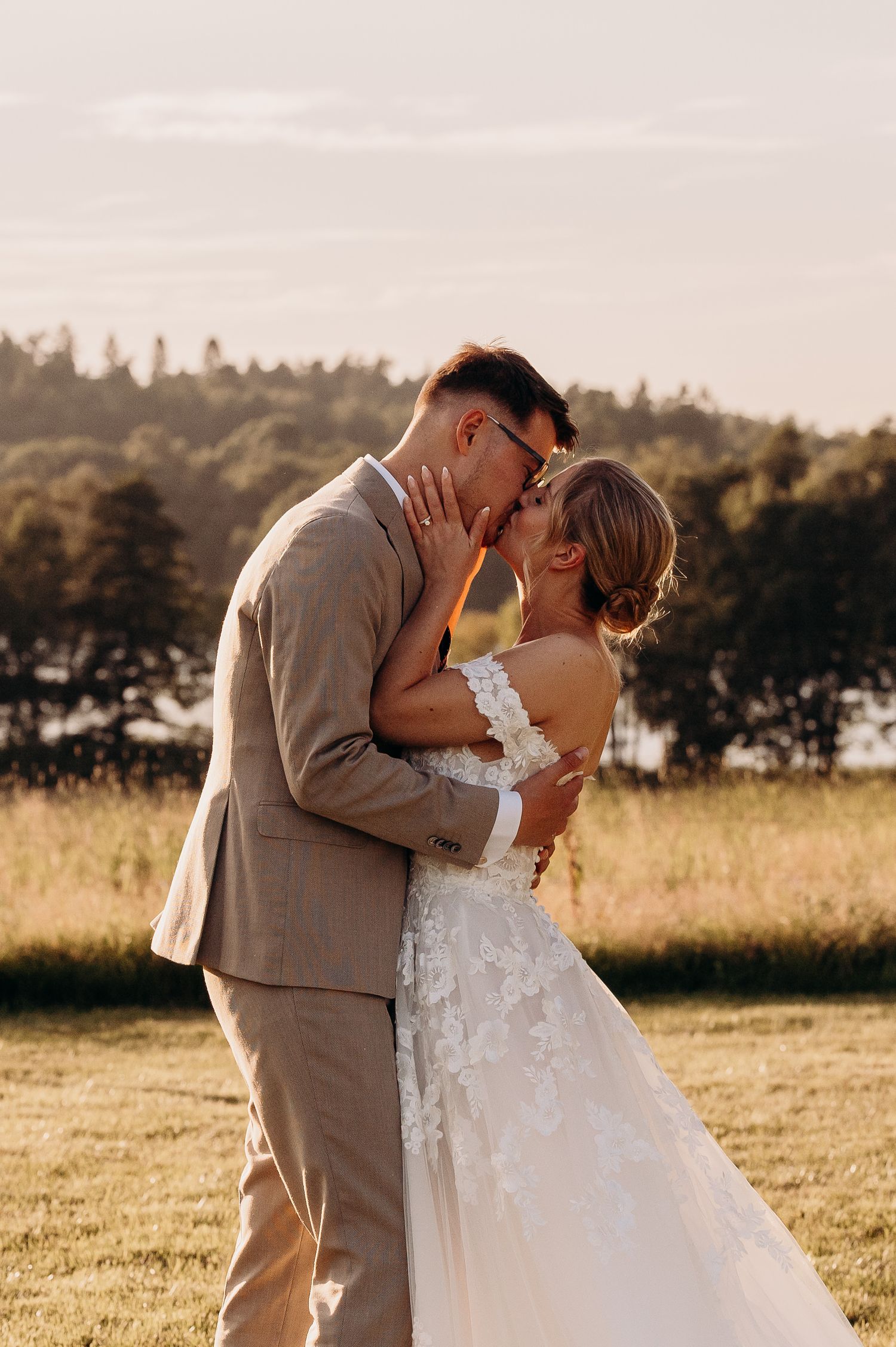 Bride and groom sharing a golden hour kiss in a sunlit outdoor field.