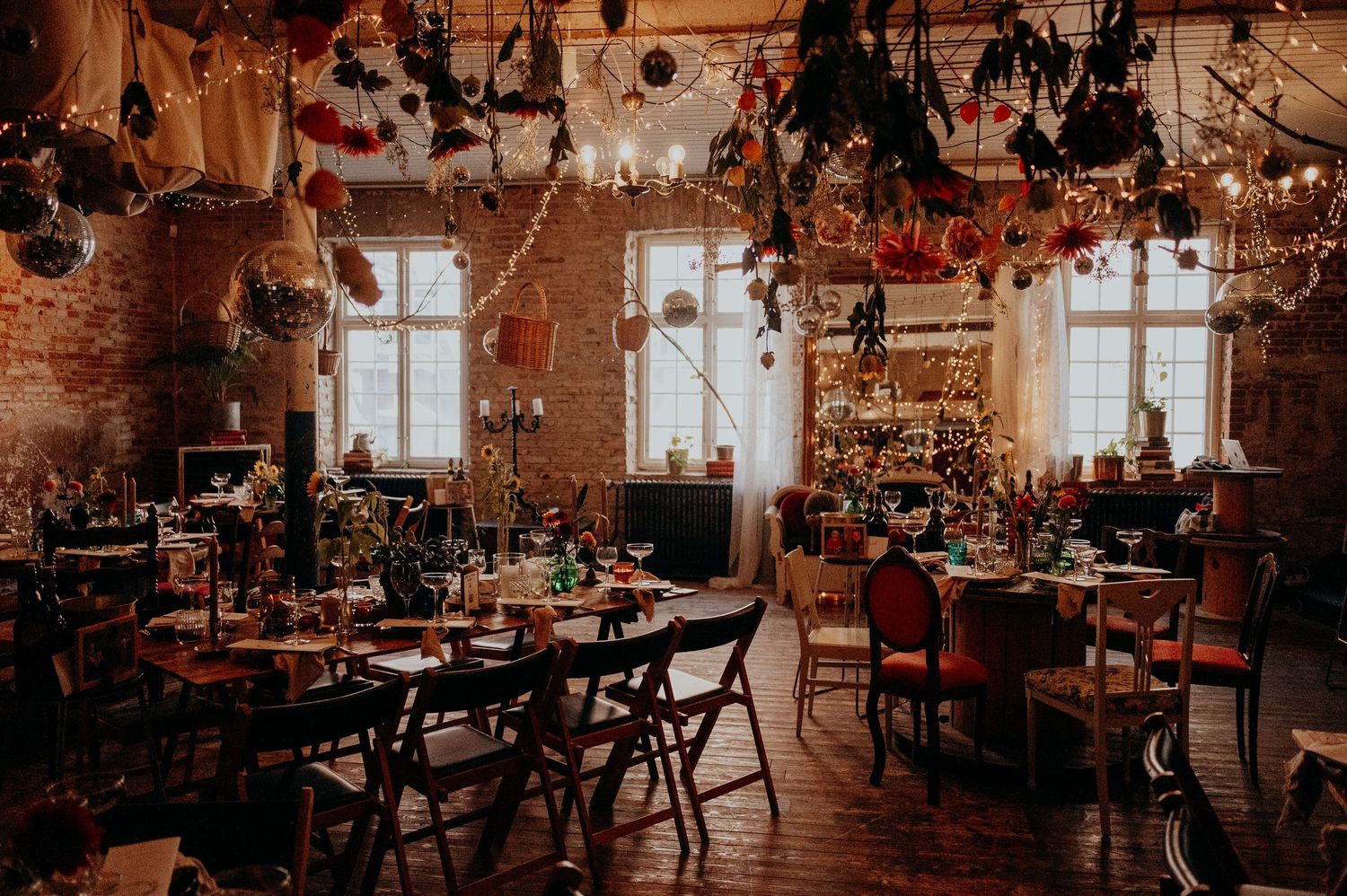 Bohemian wedding reception in rustic brick venue with hanging dried florals and eclectic table decor.