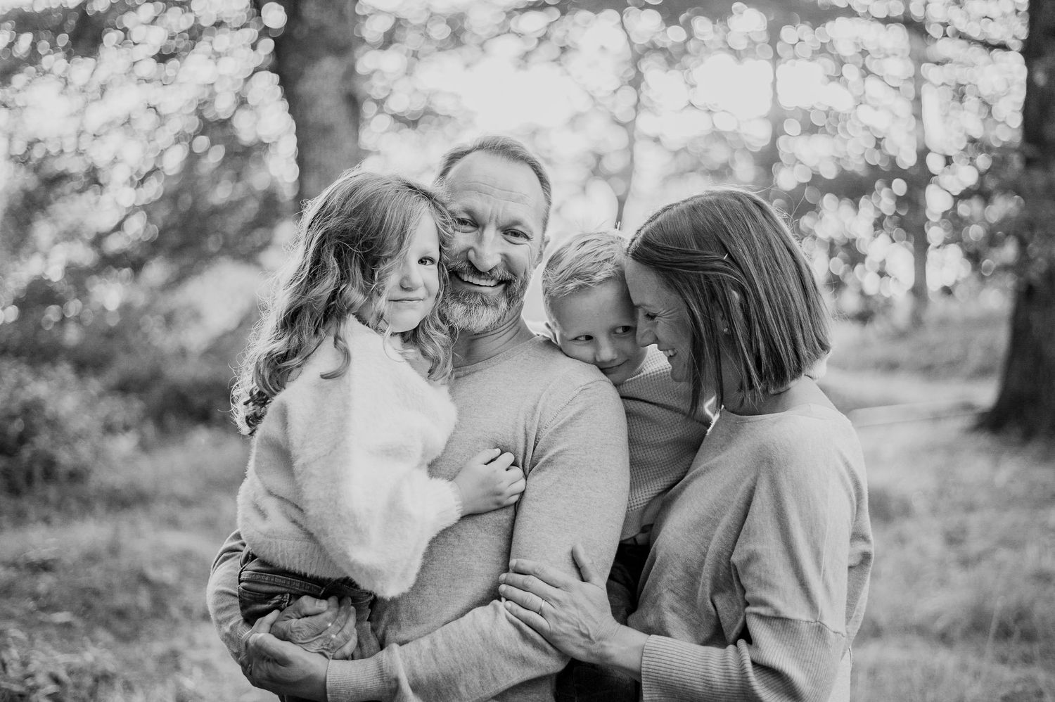 Black and white photo of a joyful father holding two young children with mother nearby.