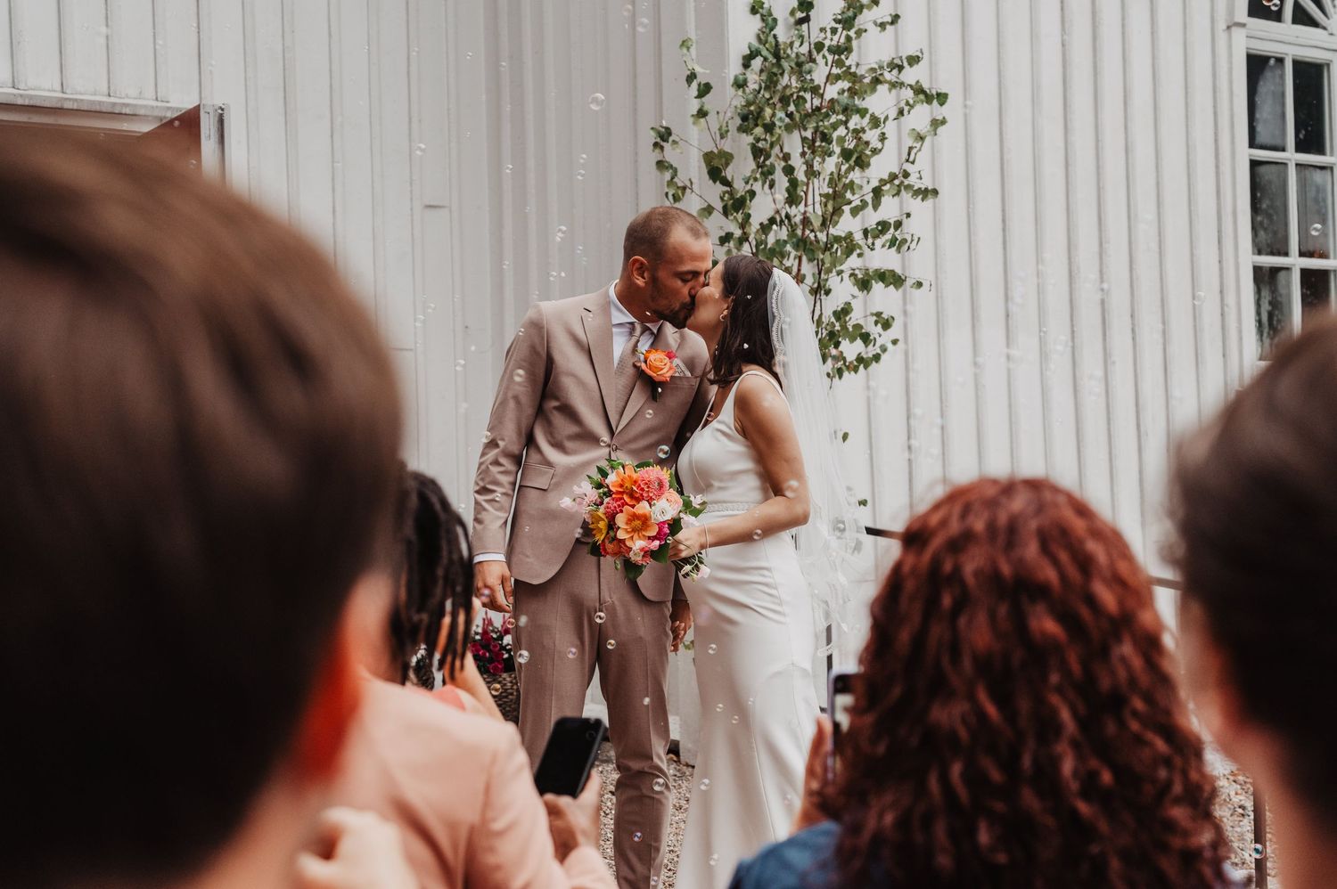 Newlyweds share a kiss during outdoor ceremony as guests celebrate with confetti.