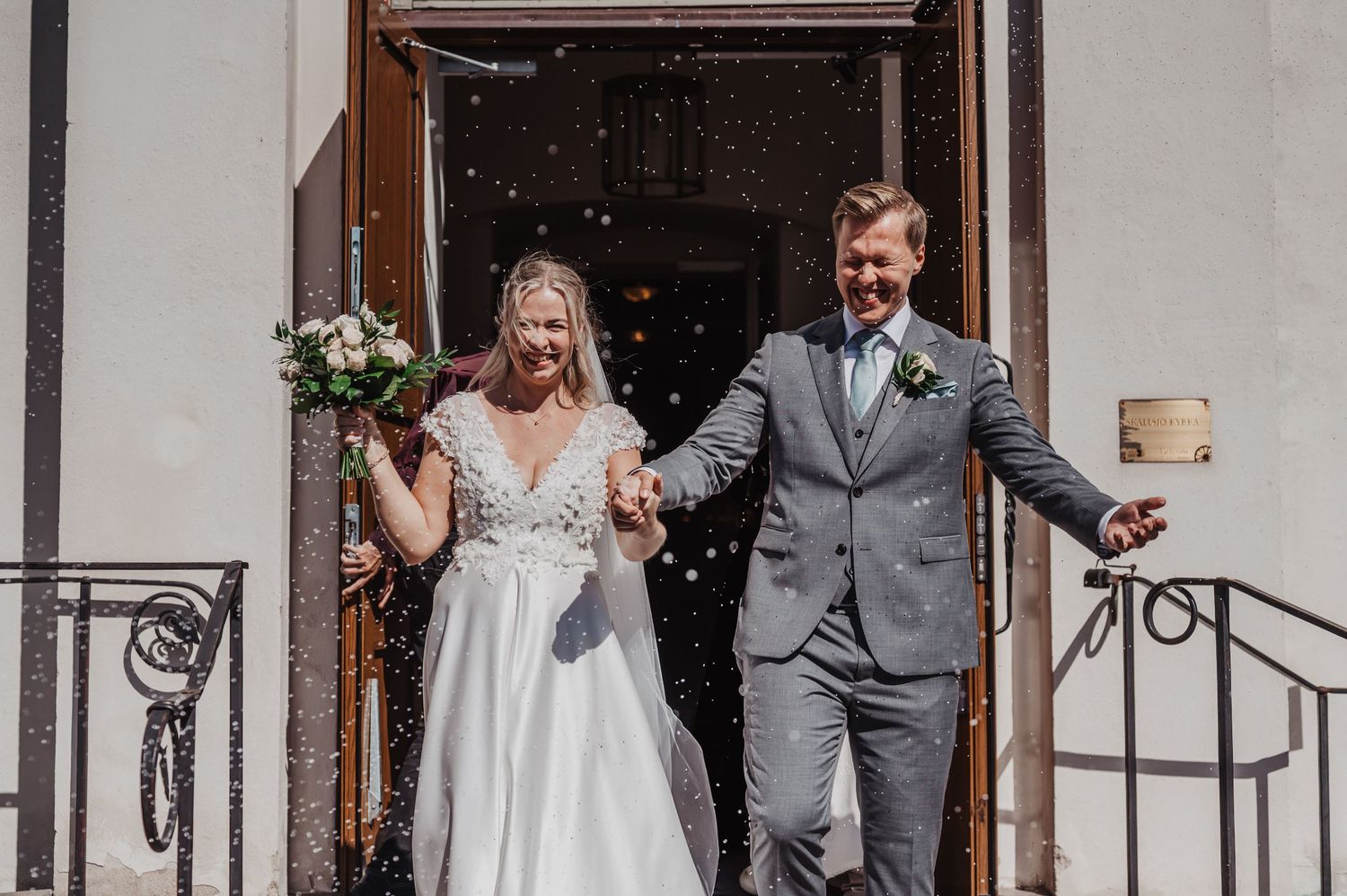 Newlyweds exit church doors hand in hand as guests shower them with confetti in joyful celebration.