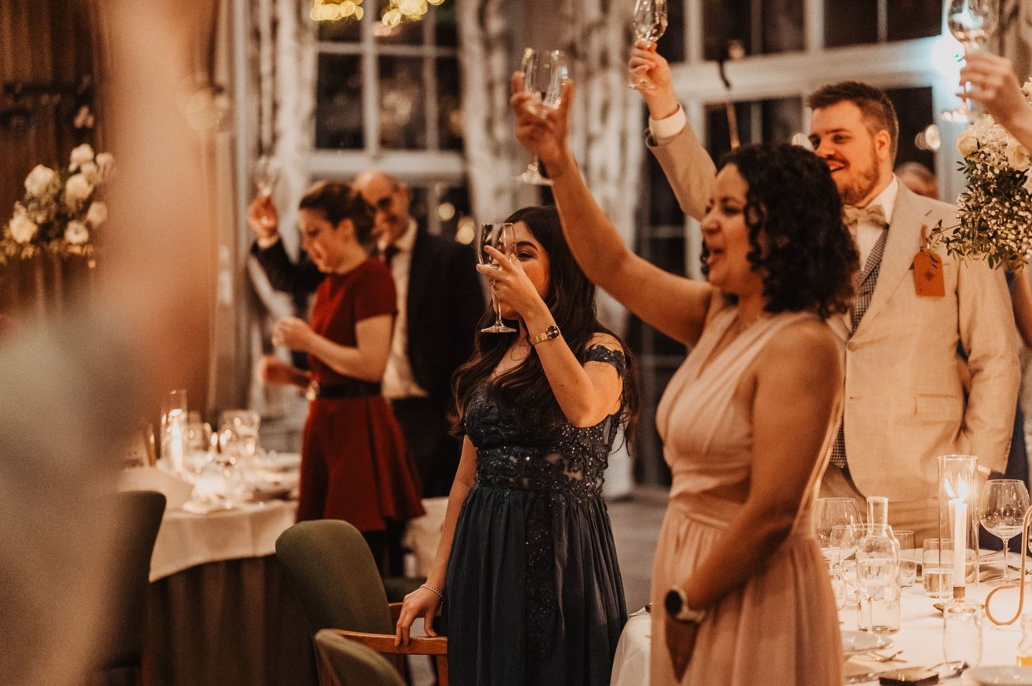 Wedding guests dance and celebrate at an elegant reception with warm lighting and decorative floral arrangements.