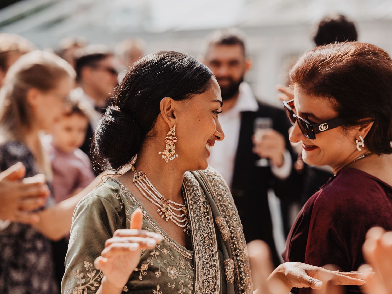 Two women in elegant Indian attire share a joyful dance at a festive outdoor celebration.