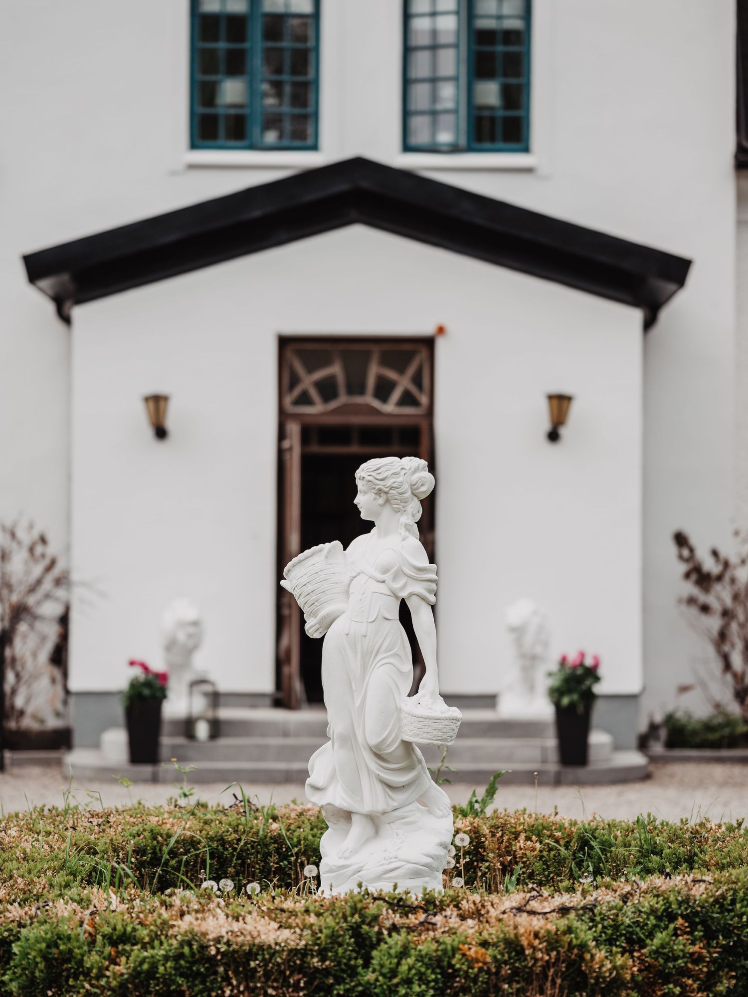 A classical white female statue stands in a garden in front of a white wedding venue entrance.