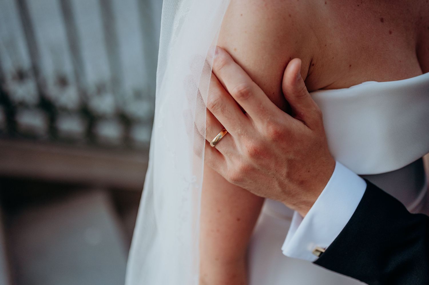 Close-up of a bride and groom embracing, showcasing a delicate gold wedding ring on the brides hand.