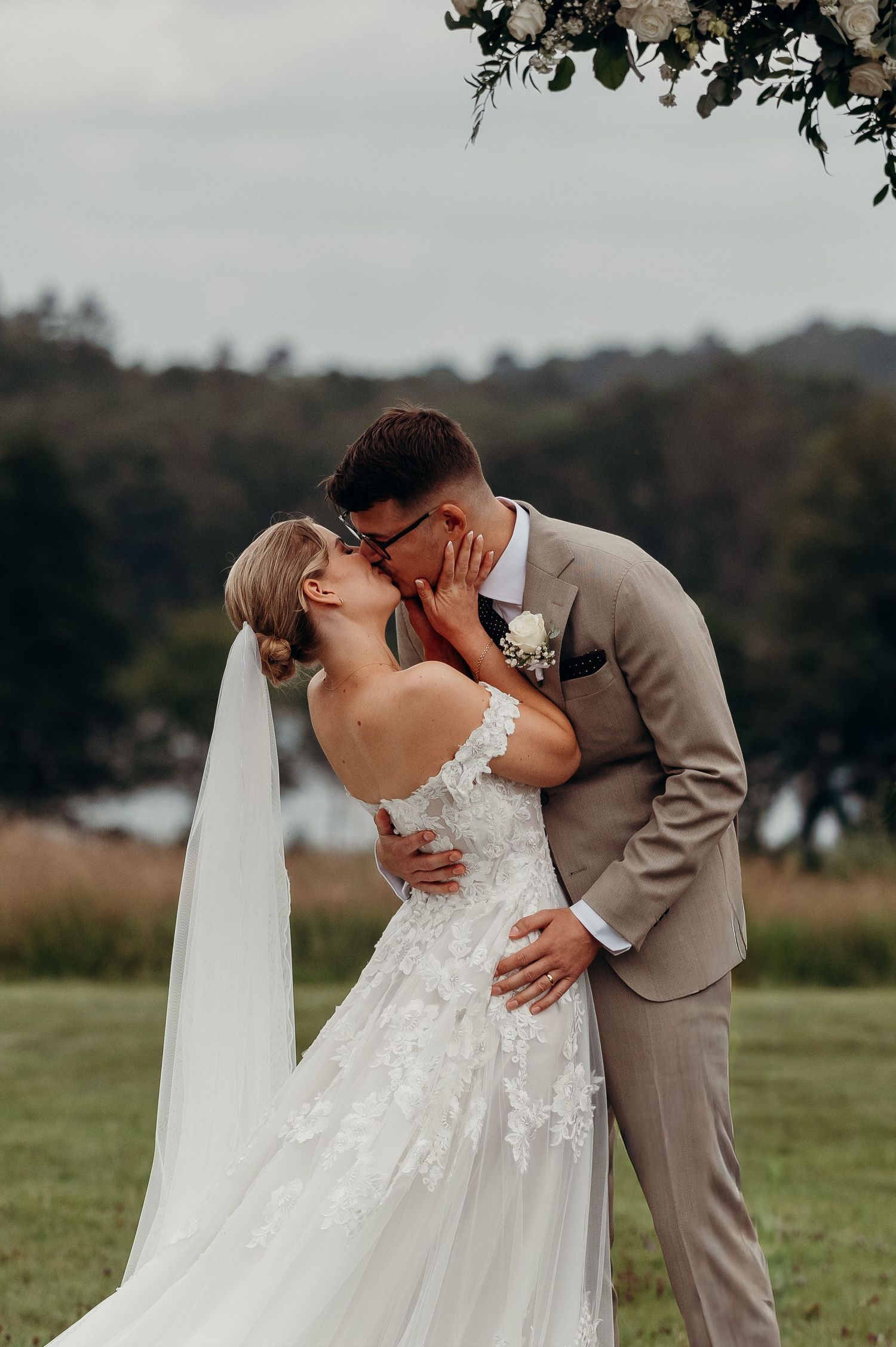 Bride and groom share a first kiss under a floral arch in an outdoor wedding ceremony.