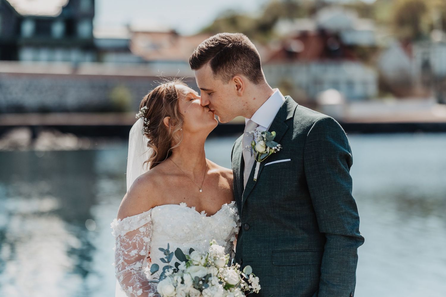 Bride and groom sharing a romantic kiss on a waterfront dock on their wedding day.