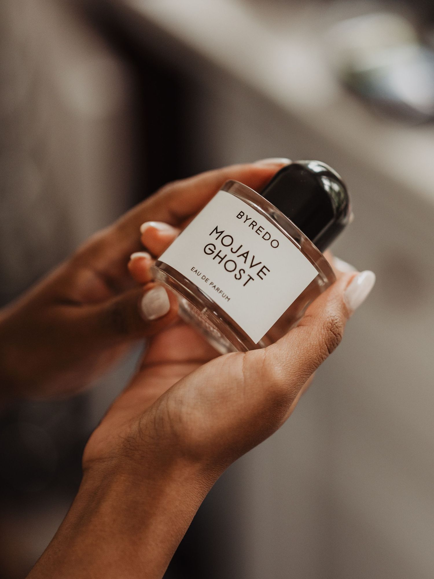 Hands holding a bottle of Byredo Mojave Ghost Eau de Parfum during bridal wedding preparations.