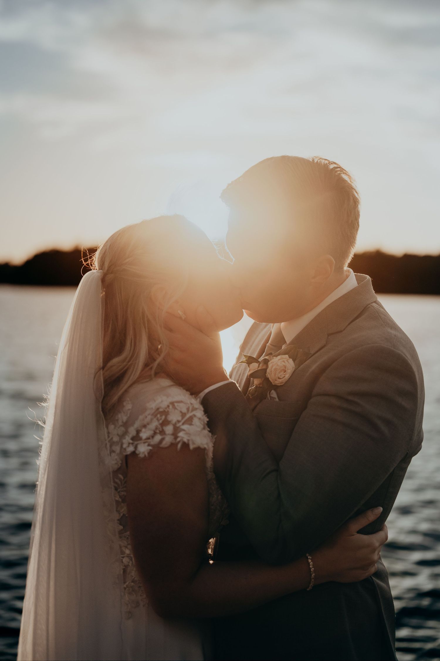 Bride and groom share a romantic sunset kiss by the water on their wedding day.