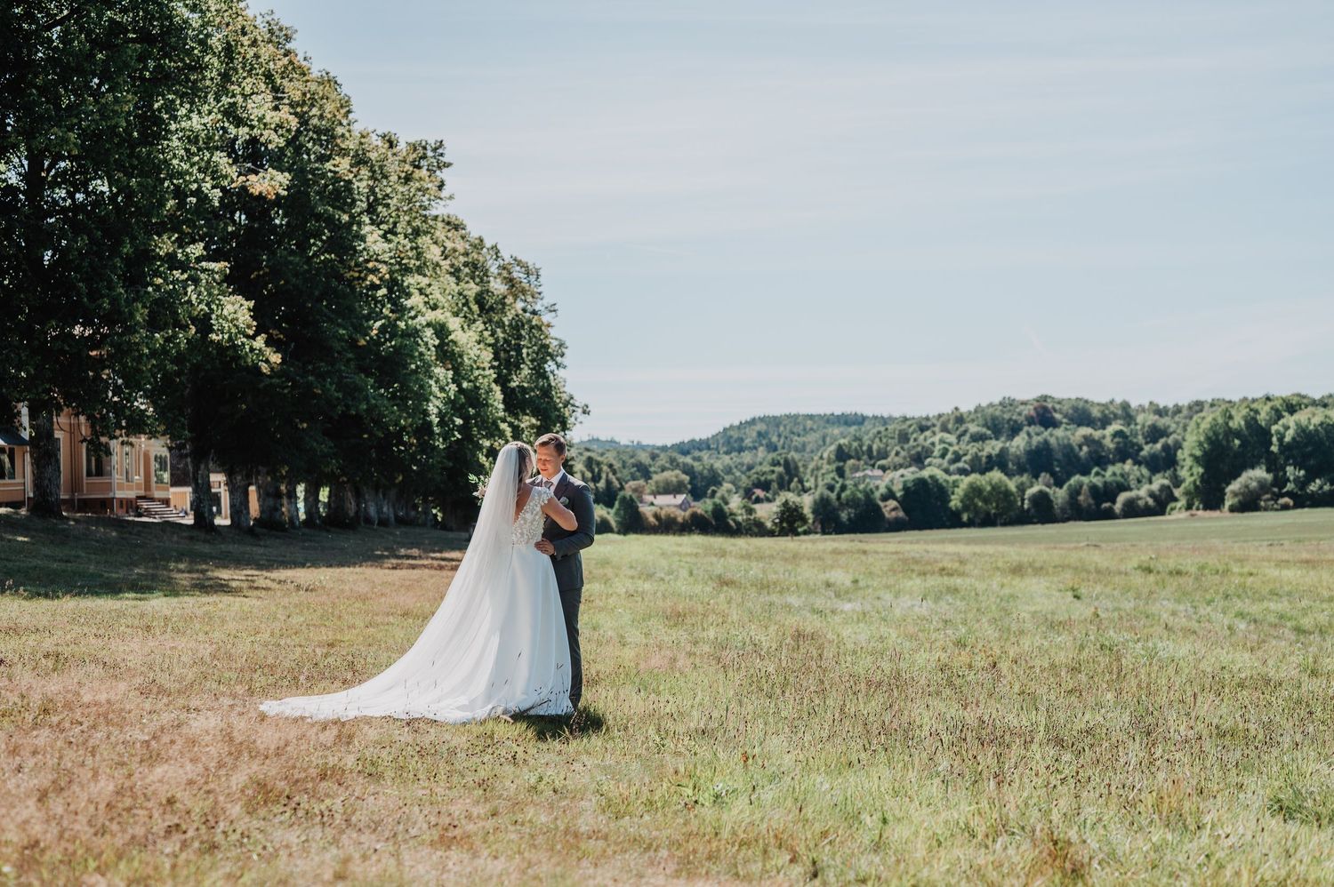 Bride and groom sharing a romantic kiss in a lush green meadow on their wedding day.