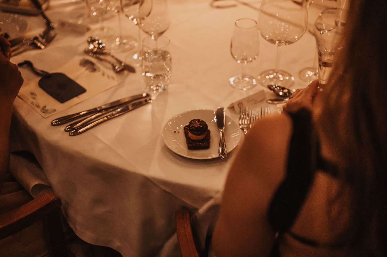 Elegant restaurant table setting with wine glasses, silverware, and a chocolate dessert on white linen.