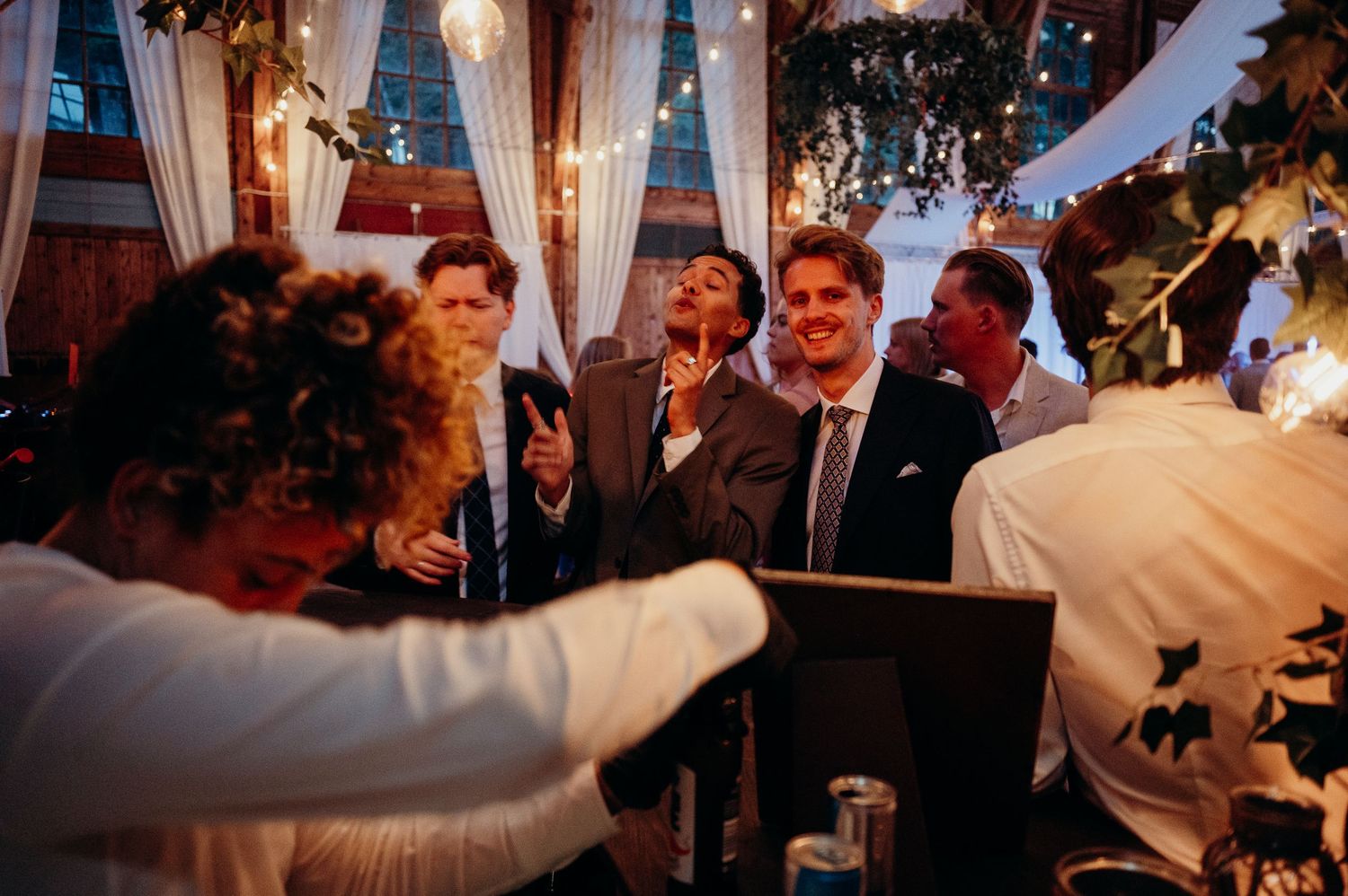 Wedding guests laugh and celebrate together at a warmly lit indoor wedding reception.