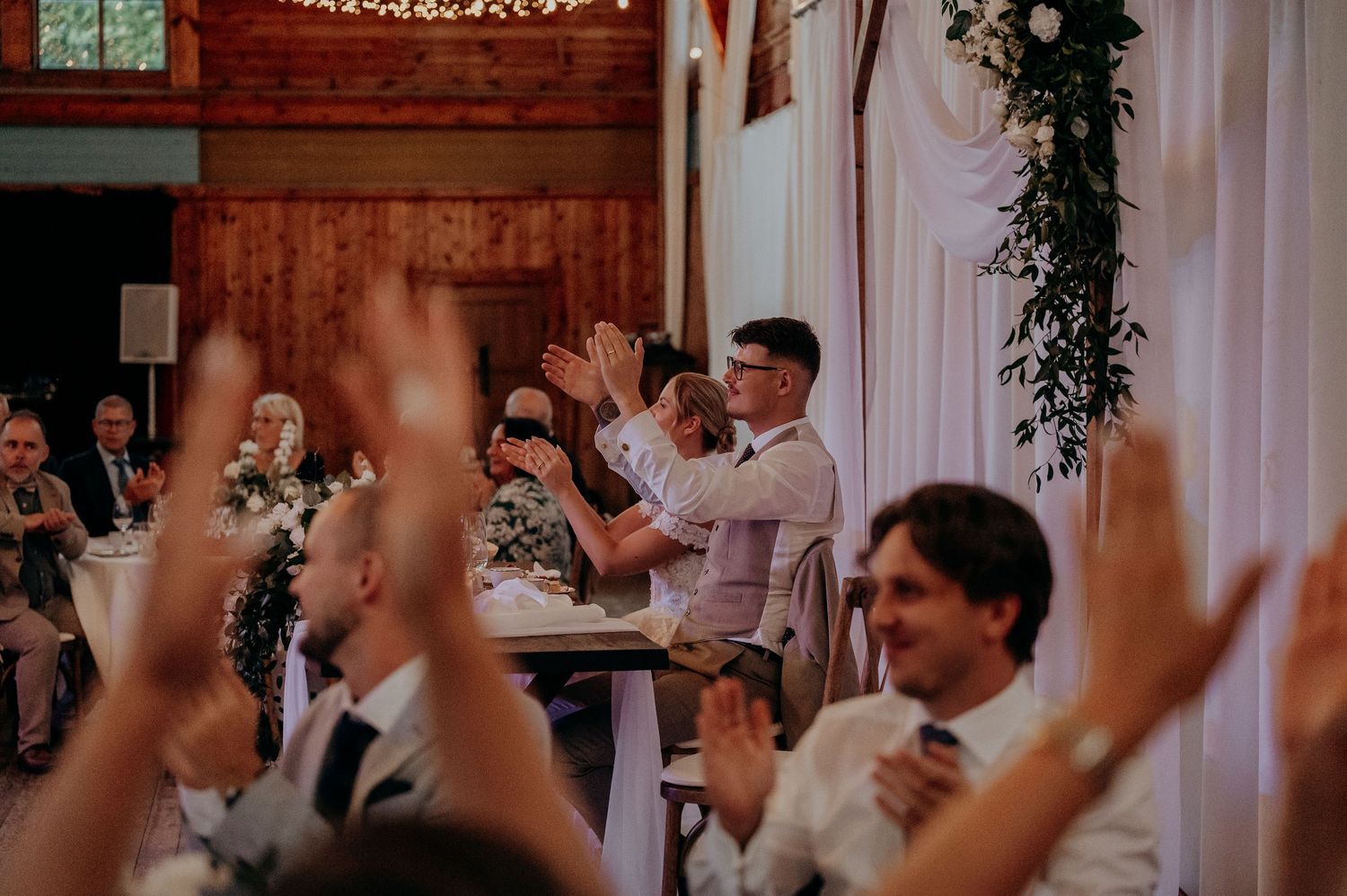 Wedding guests raising hands cheering at bride and groom during barn reception.